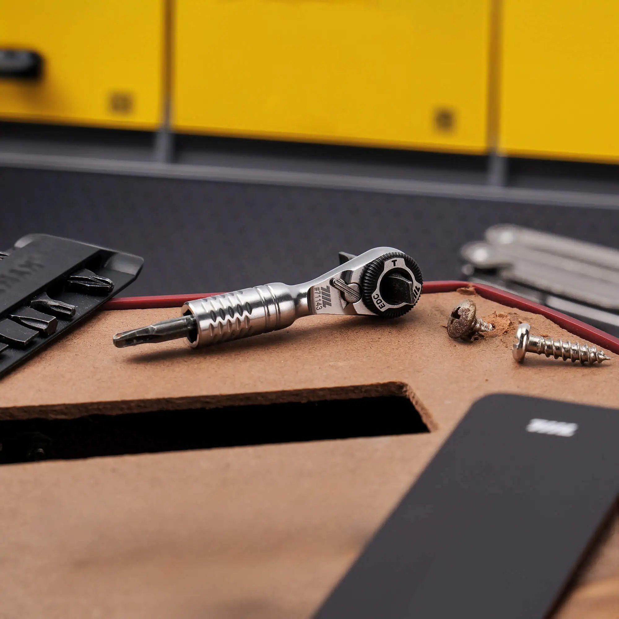 711L Mini Ratchet Wrench TG on a wooden workbench beside a smartphone and loose bits